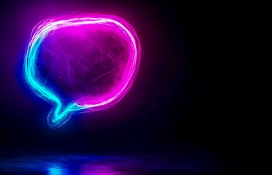 Glowing neon speech bubble reflecting on dark surface Vibrant neon speech bubble, illuminated in pink and blue hues, hovers above a dark reflective surface, creating a striking visual against the black backdrop